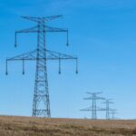 Hochspannungsmasten auf einer trockenen Hügellandschaft unter blauem Himmel
