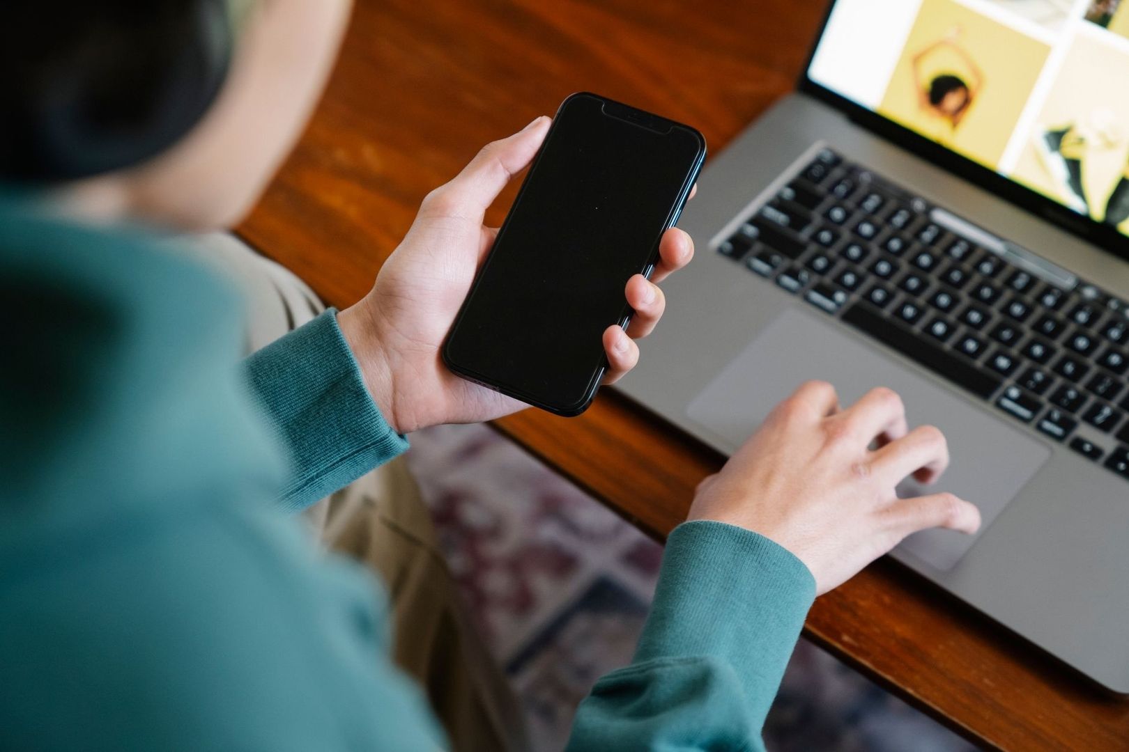 Person hält ein Smartphone neben einem Laptop mit sichtbaren Medieninhalten